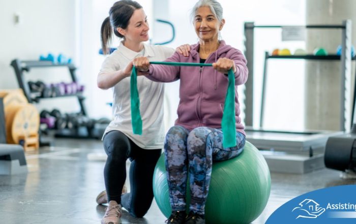 A care provider helps an older woman exercise with a resistance band and an exercise ball, representing how exercise can help with senior fall prevention.