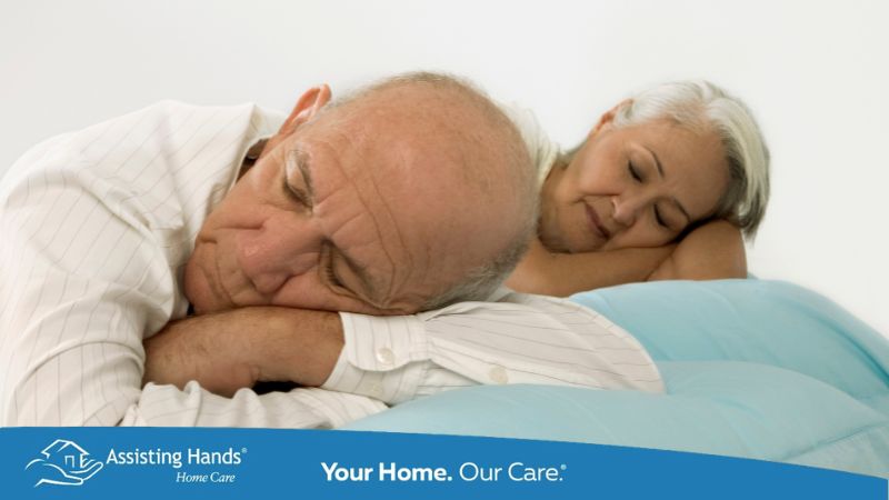 A senior man sleeping comfortably on his left side in bed with a knee pillow placed between his legs for support and spinal alignment in a calm bedroom setting.