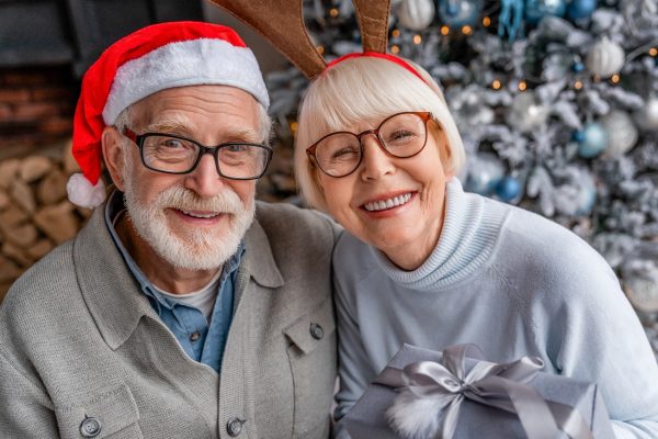 Senior couple with present box sitting in front of Christmas tree and looking in camera