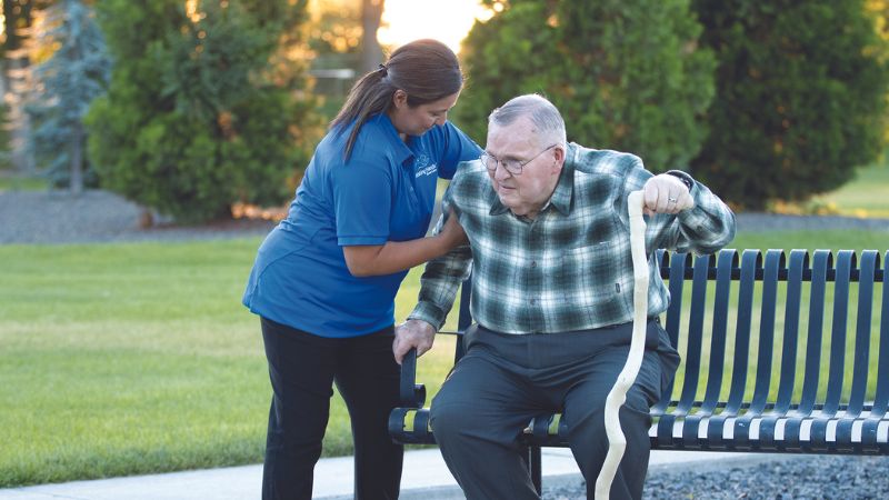 assisting hands caregiver helping senior man sit on the bench who has severe osteoporosis