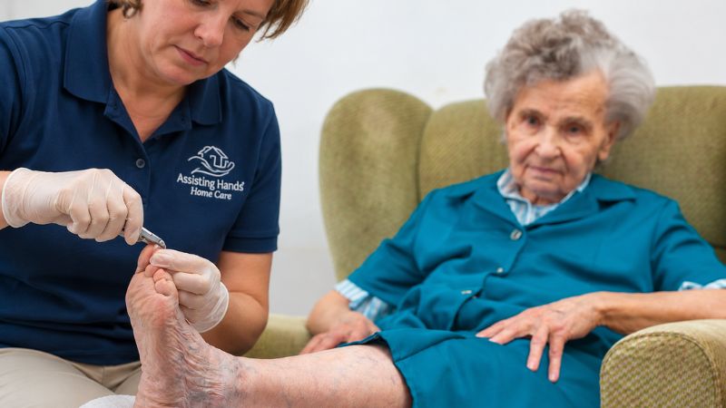 Assisting Hands Caregiver Cutting Senior Woman's Nails For Hygiene and Grooming