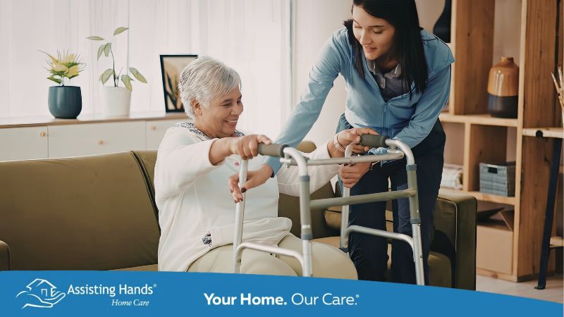 Elderly woman getting up from couch with walker and caregiver's assistance
