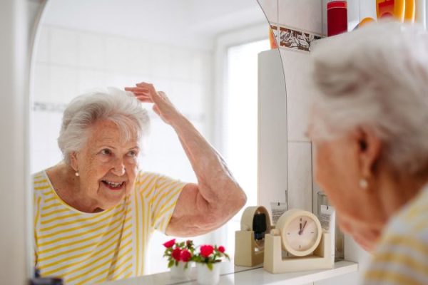Senior Woman Combing Her Hair in Bathroom and seeing if she should wash her hair or not