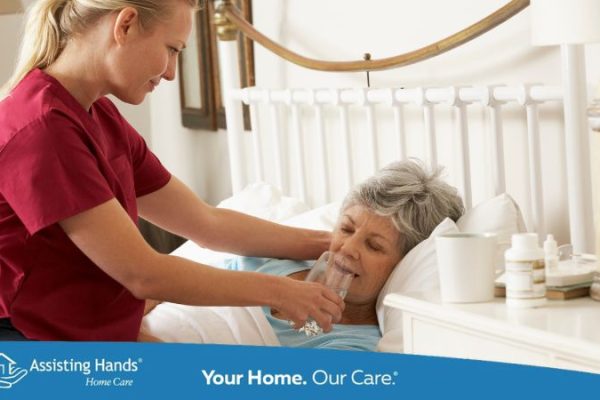 caregiver giving water to senior woman who is dehydrated and laying on bed