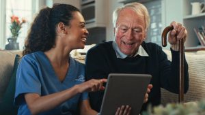 caregiver reading a book online for senior man at home in Frisco and enjoying the company