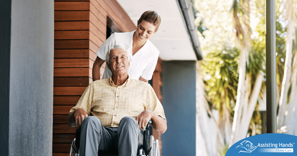 A caregiver brings an elderly man in a wheelchair out of a building, demonstrating a hospital discharge.