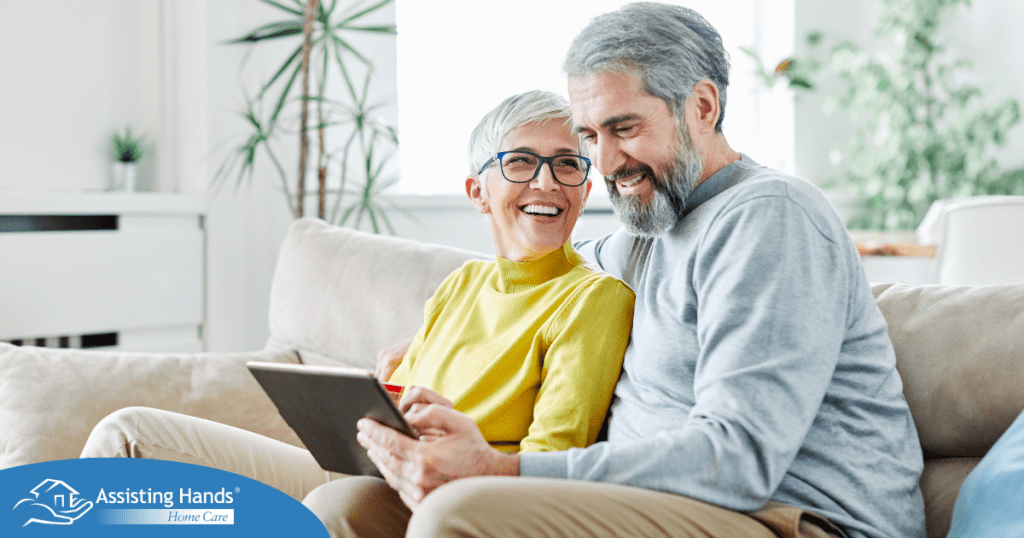 A senior couple smiles while looking at a laptop, showing how online resources can help family caregivers.