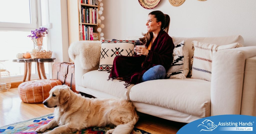 A woman relaxes with her dog while sipping on tea, representing how self-care can combat caregiver stress.