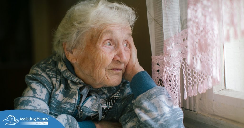 An older woman peacefully looks out of the window while the sun is still up, representing what can happen with sundowning.