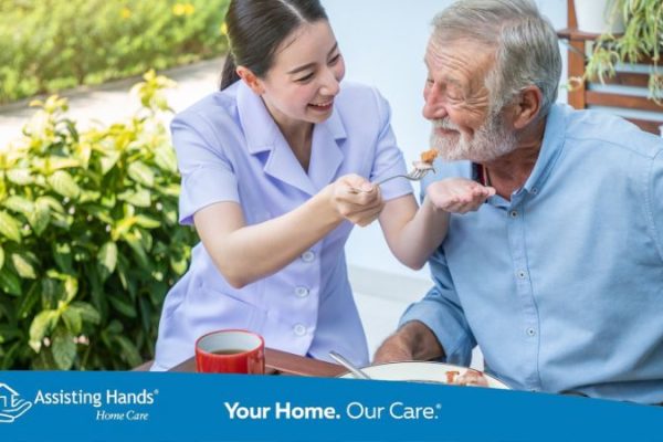 Caregiver helping senior with Alzheimer’s eat a healthy meal at home